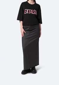 Černé oversized tričko s potiskem "EXTASIA" v růžové barvě. Černá přiléhavá maxi sukně ze hladkého materiálu. Silné černé platformové boty.
