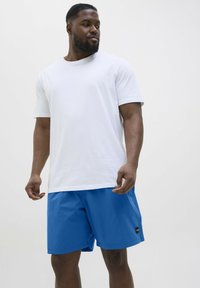 Witte katoenen T-shirt met korte mouwen, gecombineerd met felblauwe shorts. De shorts hebben een klein zwart labeldetails. Eenvoudig, casual ontwerp.