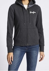 Sudadera con capucha gris oscuro con cremallera, capucha con cordón, bolsillos delanteros y un detalle de logo en blanco. Tela suave, diseño ajustado y puños acanalados.