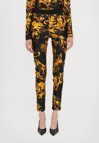Black leggings with a bold yellow and gold swirling floral pattern, made from a smooth fabric, featuring a fitted design and a high waistband.