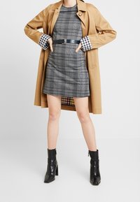 Vaaleanruskea trenssitakki harmaan ruutukuvioisen mekon päällä, korostettuna mustalla vyöllä. Mustat nilkkurit, joissa on terävä kärki. Pukeissa on ruutukuvioiset kalvosimet.