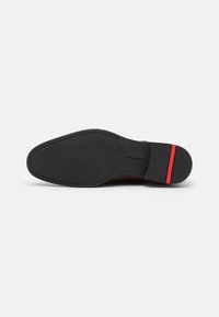 Semelle noire d'une chaussure avec une texture lisse, une forme légèrement courbée et un accent rouge au niveau du talon.