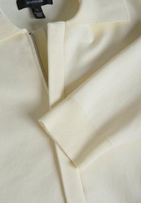 Top tricotat de culoare galben deschis, cu închidere cu fermoar și guler, având o textură ribbed la manșete și la tiv, fabricat dintr-un material moale.