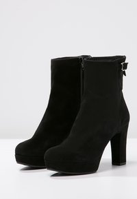 Black suede ankle boots with a high block heel, rounded toe, side zipper, and adjustable strap detail at the ankle.