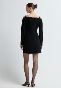 Mustapaitainen pitkähiha dressi, jossa on olkapäät paljastava muotoilu, sovitettu malli ja takana vetoketju; yhdistettynä läpinäkyviin mustiin sukkahousuihin ja mustiin korkokenkiin.