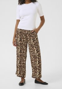 Pantalons larges à imprimé léopard en beige et brun, fabriqués en tissu doux. Assortis avec un haut blanc ajusté et des ballerines noires.