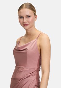 Robe en satin rose avec fines bretelles, décolleté à bavolet et drapé sur la jupe. Texture lisse et design ajusté.