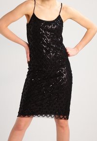 Černé flitrové šaty s přiléhavým siluetou, s diamantovým vzorem, tenkými ramínky a zvlněným lemem.