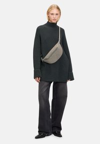 Maglione grigio a collo alto abbinato a jeans larghi grigi scuri. Una borsa curva grigia è indossata a tracolla, mostrando una texture liscia.