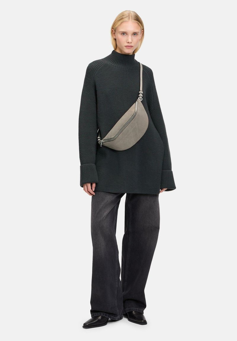 Maglione grigio a collo alto abbinato a jeans larghi grigi scuri. Una borsa curva grigia è indossata a tracolla, mostrando una texture liscia.