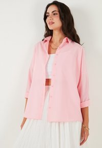 Light pink button-up shirt with a collared neckline, long sleeves rolled to the elbows, and a relaxed fit. Soft, smooth fabric texture.