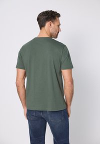 Zelené krátké tričko s kulatým výstřihem a hladkou texturou z bavlny, doplněné tmavě modrými džínami.