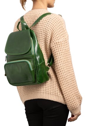 Groene leren rugzak met een gladde afwerking, voorzien van een voorvak, schouderbanden en een klepafsluiting. Gedragen op een beige trui.