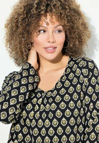Schwarze Bluse mit einem gemusterten Design in Grün und Weiß, V-Ausschnitt, langen Ärmeln und zarten floralen Motiven.