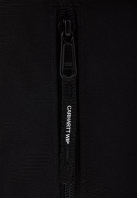 Giacca nera con zip YKK, realizzata in un tessuto testurizzato. La linguetta della zip riporta la scritta "CARHARTT WIP" stampata in bianco.
