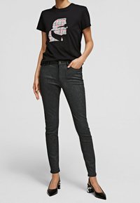 Camiseta negra con un gráfico de cuadros coloridos, combinada con unos jeans ajustados negros con brillo y unos tacones negros de punta.