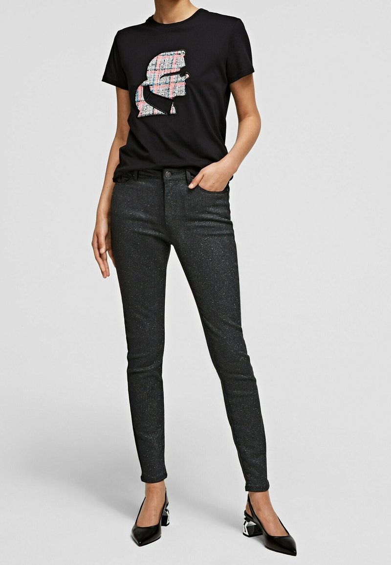 Camiseta negra con un gráfico de cuadros coloridos, combinada con unos jeans ajustados negros con brillo y unos tacones negros de punta.