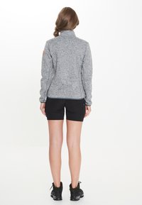 Grå fleecejacka med hög krage, slim fit-design och läderlogotyp på axeln. Kombineras med svarta träningsshorts och skor.