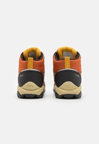 Chaussures de randonnée imperméables rouges et orange avec des accents noirs et des semelles texturées, dotées d'une languette et d'un col rembourré pour le confort.