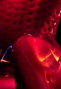 Nahaufnahme einer glänzenden roten Oberfläche mit strukturierten Dellen, die orange und gelbe Lichtreflexe reflektiert.