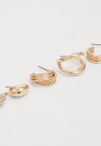 Quatre paires de boucles d'oreilles en or, avec des designs lisses, torsadés et texturés, dont une paire ornée de petits cristaux transparents.