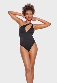 Maillot de baño negro de una pieza con un diseño asimétrico y un corte en forma de llave, textura suave y silueta ajustada.