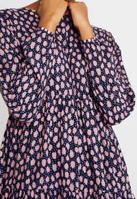 Mörkblå klänning med långa ärmar, prydd med ett mönster av rosa och blå prickar, med resår i midjan och mjukt, strukturert tyg.