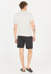 Ljusgrå bomullströja, svarta shorts, synlig tatuering på armen, lös passform, avslappnade sandaler. Neutrala färger och enkel design.