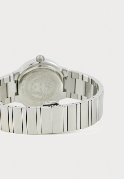 Ασημένιο ρολόι από ανοξείδωτο ατσάλι με γυαλιστερό βραχιόλι, που διαθέτει κυκλικό κάσα και εγχαραγμένο πίσω μέρος. Σημαντικά αξεσουάρ περιλαμβάνουν μια κορώνα.