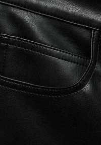 Černá kožená textura s detailním záběrem na zadní kapsu. Vyznačuje se zakřivenými okraji a viditelným šitím, což zdůrazňuje hladký, leštěný vzhled.