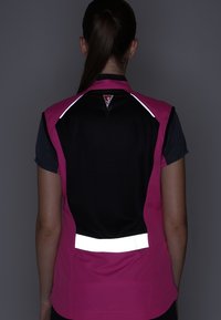 Femme avec une queue de cheval portant un gilet sans manches noir et rose avec des bandes réfléchissantes sur le haut et le bas du dos, de dos.