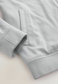 Light grey sweatshirt sleeve with ribbed cuff and a front pocket detail on soft fabric background.