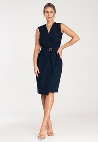Granatowa, bezrękawna sukienka typu wrap z paskiem w talii z okrągłą klamrą. Gładki materiał o dopasowanym kroju.