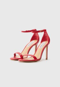 Sandales à talons hauts rouges avec des brides, à finition brillante, dotées d'une fine sangle autour de la cheville, d'un design ouvert et d'un talon aiguille mince.