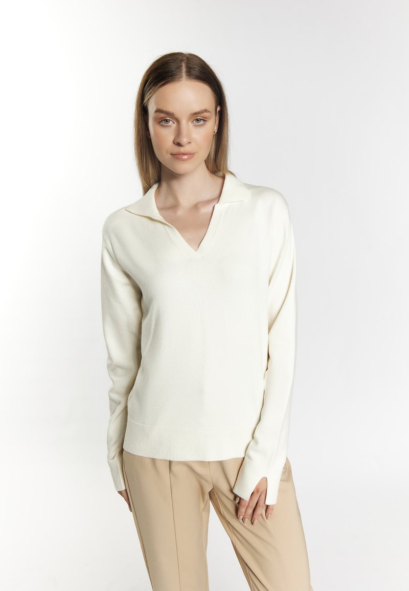 Ivory knit sweater with a V-neck and collar, featuring long sleeves and ribbed hem. Paired with beige trousers. Smooth texture.