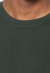 T-shirt vert foncé à col ras du cou avec une texture lisse et un col côtelé. Gros plan montrant l'encolure et les détails du tissu.