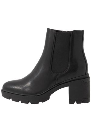 Bottine en cuir noir avec des panneaux latéraux élastiques, un talon épais et une semelle en caoutchouc robuste avec un motif en zigzag.