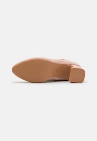 Rosa semsket hæl med en teksturert overdel, glatt tå og solid gummisåle. Har blokkhæl for stabilitet. Enkel og ren design.