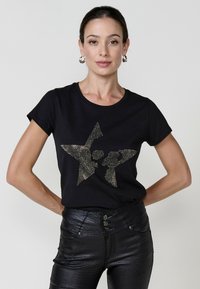 Zwarte T-shirt met korte mouwen, versierd met een textuur ster ontwerp van gouden schitterende steentjes, gecombineerd met glanzende zwarte broek.