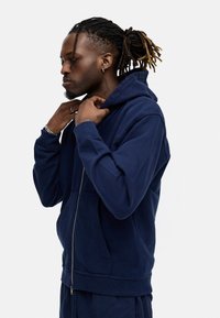 Navy blue zip-up hoodie with a front pocket, long sleeves, and adjustable drawstring hood. Made of soft fabric with ribbed cuffs.