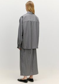 Graues Zweiteiler-Outfit mit einer lockeren Knopfleiste-Hemdbluse und einem passenden langen Rock. Glatter Stoff, minimales Design und flache schwarze Schuhe.