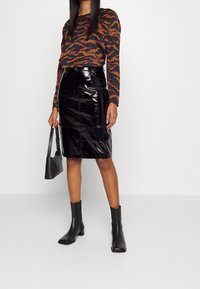 Haut à manches longues avec un motif zèbre en marron et noir, associé à une jupe en cuir verni noire taille haute et des bottines noires.