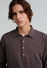 Long-sleeve, button-up shirt in dark gray corduroy fabric. Features a classic collar and five front buttons. Smooth texture and relaxed fit.