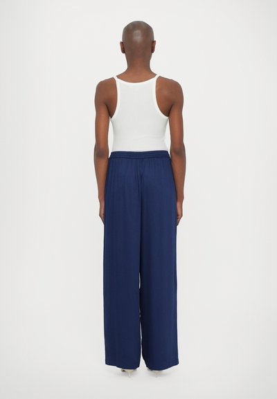 White tank top with narrow straps and navy wide-leg trousers featuring an elastic waistband. Smooth texture, casual design, full-length pants.