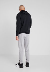 Felpa nera con cappuccio abbinata a pantaloni grigi. La felpa presenta una vestibilità comoda e polsini a costine, mentre i pantaloni hanno tasche laterali e gamba affusolata.