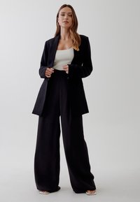 Černý blazer a kalhoty s širokými nohavicemi z měkké, splývavé látky. Vrchní díl má přiléhavý, ribbovaný design v světlé zelené barvě. Minimalistický styl.