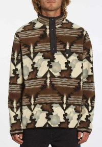 Pullover en polaire avec un col élevé, présentant un motif géométrique marron, crème et gris, une fermeture à pression et un patch logo sur la poitrine.