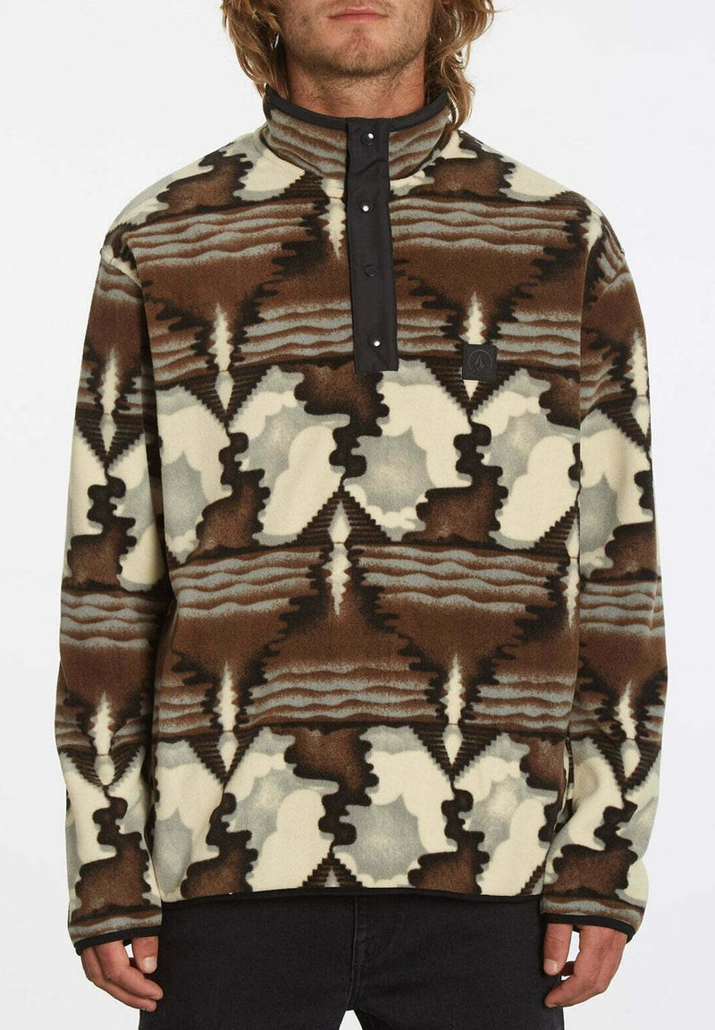 Pullover en polaire avec un col élevé, présentant un motif géométrique marron, crème et gris, une fermeture à pression et un patch logo sur la poitrine.