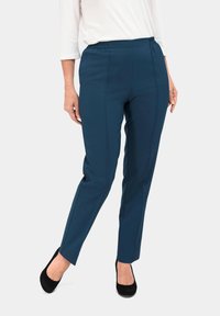 Donkerblauwe stretchbroek met een elastische tailleband, taps toelopend ontwerp en verticale stikdetails; gecombineerd met zwarte hoge hakken.