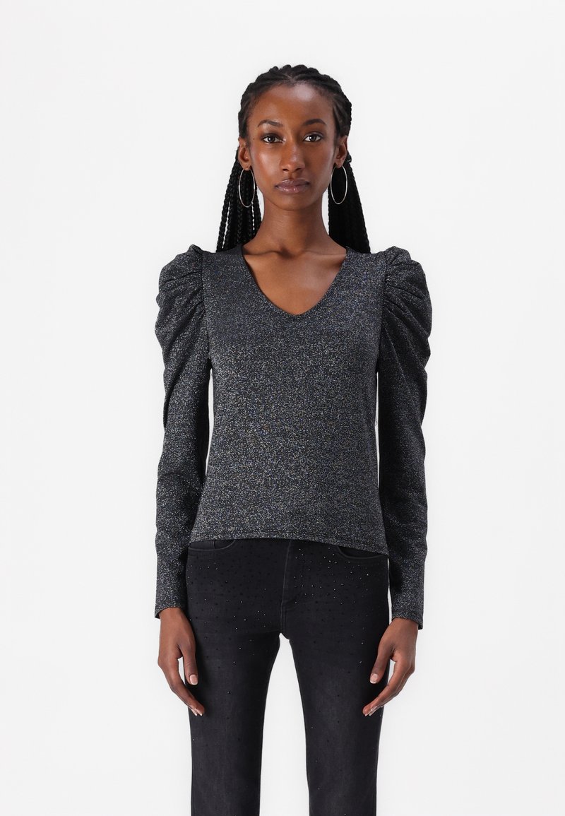 Black, sparkly long-sleeve top with a V-neck and puffed shoulders. Paired with black jeans featuring subtle embellishments.
